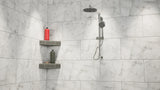 A wide view of a white-marbled standing shower with a rainfall shower head mounted on the wall next to an original corner shower shelf covered in gray tile while holding a red shampoo bottle, a gray conditioner bottle and a bar of soap.