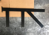 A Long Black Custom Support Bracket with two arms coming down vertically and one arm with a 45-degree angle from the top, sitting on a cardboard box on a cement floor.