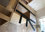 Top-down angle of Black Custom Support Brackets sitting on an unfinished wooden countertop with a white work table in the background.
