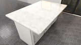 A top-down view of a white marble island countertop with cabinets for storage on a gray tile floor.